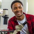 student posing for a photo with a microscope. 