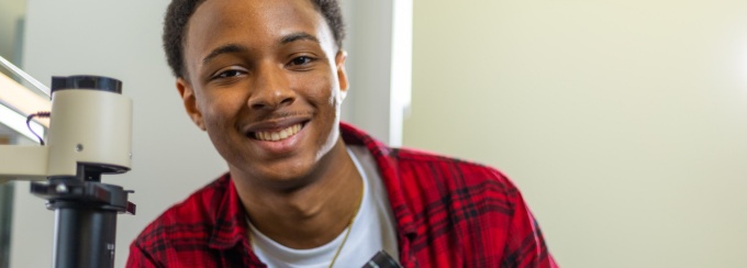 student posing for a photo with a microscope. 