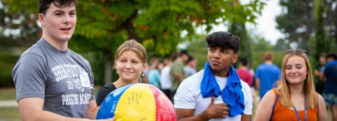 students standing outside, one holding a colorful beach ball. 