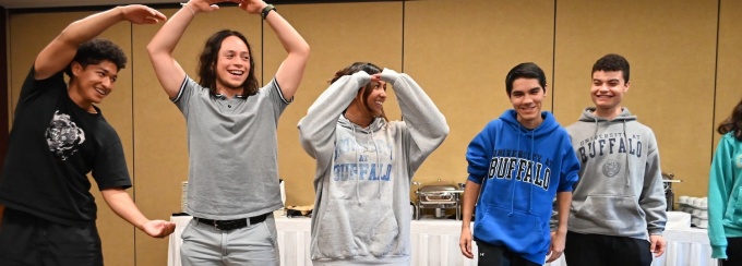 students making letter shapes with their bodies while indoors at an event. 