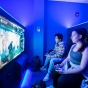 two students in a dark room playing a video game on a big screen. 
