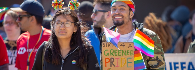 A diverse group of students at the 2019 UB pride parade. The man in front holds a sign that says strive for a greener pride. 