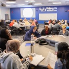Image of students in a classroom at a round table having a discussion. 