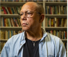 man with glasses with books in the background. 