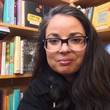 Louisa Fletcher-Pacheco smiling in front of a bookshelf. 