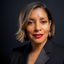 Patrice Funderburg smiling in a black blazer on a black background. 