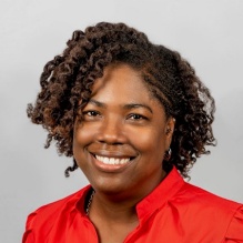 Frankie Kraft smiling in a red blouse on a grey background. 