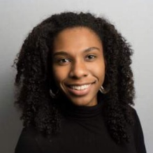 Dr. Amani Johnson smiling in a black turtleneck on a grey background. 