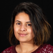 Kristina Medero smiling in a headshot with a dark shirt in a clear dark background indoor. 