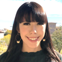 Minerva Rodriguez smiling in a headshot with a dark shirt in outside background with trees. 