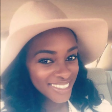 Kinyata Cooper smiling in a headshot with a white shirt and hat in a car seat. 