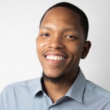 Martez Smith headshot smiling in blue and white shirt with stripes and clear background. 
