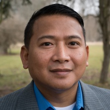 Nielson Hul headshot in a suit and outdoor background with trees. 