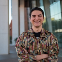 Juan Hernandez smiling in a headshot with a dark shirt with patterns in outside background with columns. 