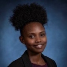 Joyline Chepkorir smiling in a headshot with dark shirt and blueclear indoor background. 
