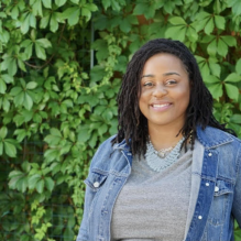 Brittany Marshall smiling in a headshot with a jean jacket and bright shirt in outside background with leafs. 