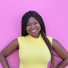 Termara Parker in a headshot smiling with bright shirt and pick background. 