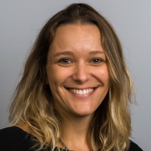 Daniela Goya-Tocchetto smiling in a headshot with dark shirt and light clear background. 