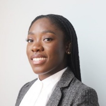 Adedoyin Inaolaji smiling in a headshot with a dark blazer and white shirt in inside background with clear gray background. 