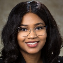 Dahlia Al-Haleem headshot smiling with dark shirt, glasses and in indoor clear background. 
