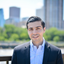 Zachariah smiling infront of a city landscape. 