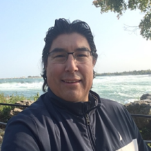 Josh Manitowabi smiling infront of a beach. 