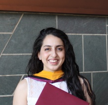 Ruth Lopez Fajardo smiling in a white dress and yellow, black, and burgundy hood on an inside background. 