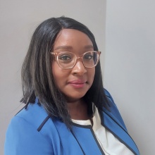 Chesney Ward smiling in a blue blazer and white shirt on a gray background. 