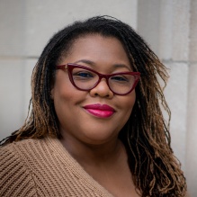 Evelyn Coker smiling in a brown sweater on an outside background. 