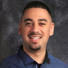 Rubén González smiling in a blue shirt with white dots on a black background. 
