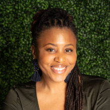 Paigean Jones smiling in a black shirt on an ivy background. 
