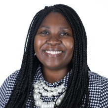 Brittani Wright smiling in a black and white checkered shirt with pearl necklaces on a white background. 