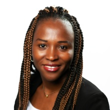 Blessing Okafor smiling in a black blazer and white shirt on a white background. 