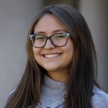 Luz Robinson smiling in a gray sweater on an outside background. 