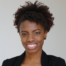 Randi Williams smiling in a black blazer on a gray background. 