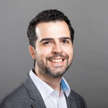 Robson Martinz de Araujo "Junior" smiling in a gray blazer and white shirt on a gray background. 