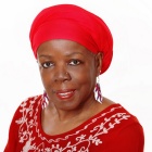 Karima Amin smiling in a red blouse and headwrap on a white background. 