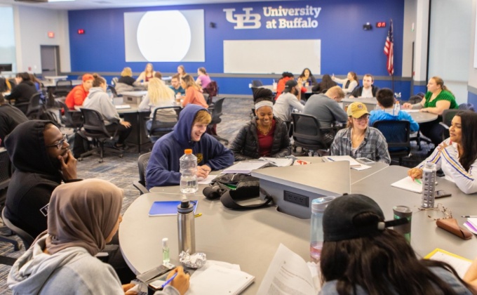 Students smiling and laughing while working together at a large circular table. 