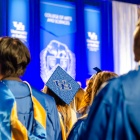 Image of students in graduation regalia at UB commencement. The students are facing away from the camera. 