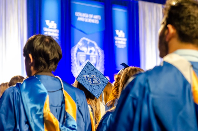 Image of students in graduation regalia at UB commencement. The students are facing away from the camera. 