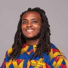 Adam McNeil smiling in a headshot with colorful shirt and gray clear background. 