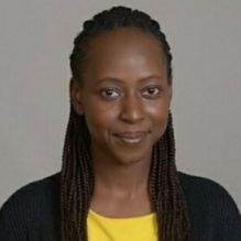 Sylvia Ayieko smiling in a yellow shirt and black cardigan on a gray background. 
