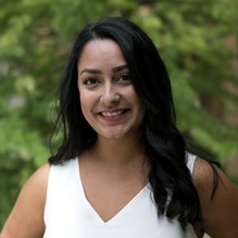 Mariela Faykoo-Martinez smiling in a headshot with a white shirt in outside background with trees. 