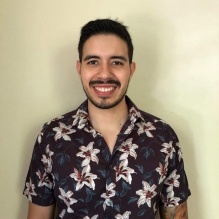 Daniel Chavarria smiling in a headshot with a dark shirt with bright floral pattern in indoor background. 