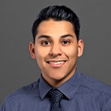 Israel Garcia-Carachure smiling in a headshot with a dark shirt and tie in indoor clear background. 