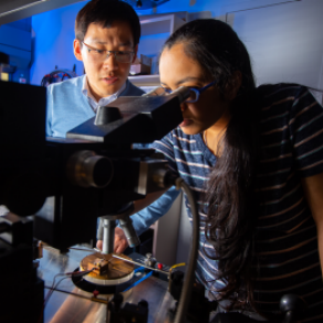 Researchers looking in microscope in CMI lab space. 