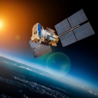 A satellite orbits the Earth with the sun in the background. 