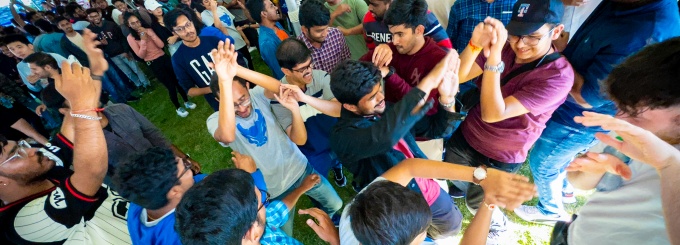 Large group of international students dancing under a big, white tent at Baird Point. 