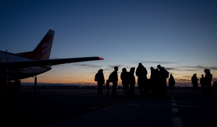 Students waiting on tarmac near airplane during sunrise. 