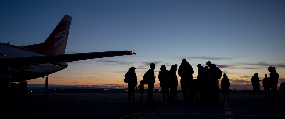 Students waiting on tarmac near airplane during sunrise. 